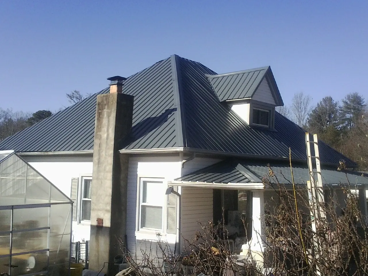 Dark blue standing seam metal roof on a white farmhouse with dormer — Slate & Tile Roof Repair by Roofing Brothers in Warrington