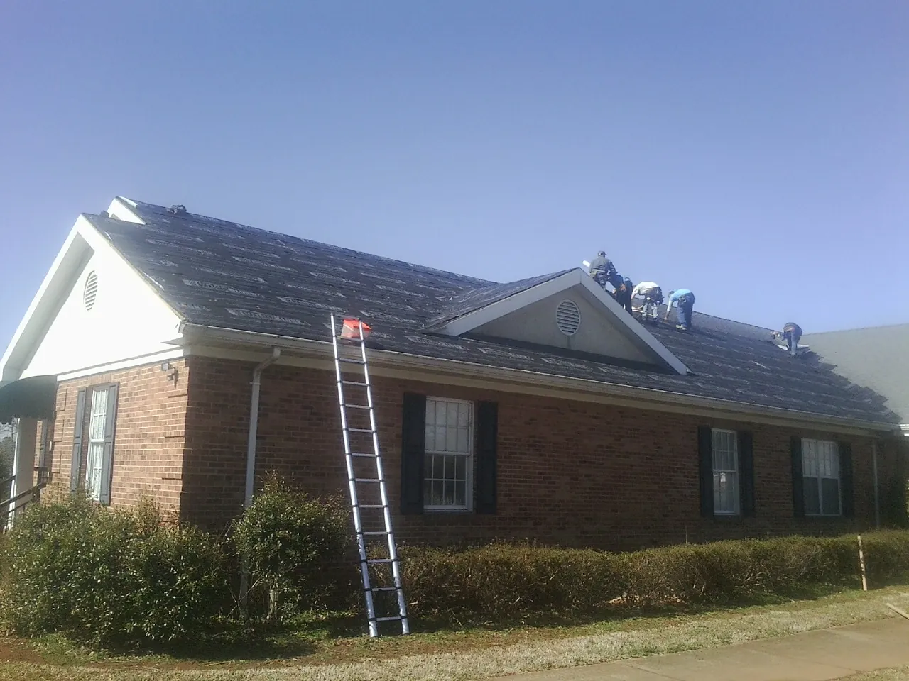 Crew tearing shingles off a brick ranch roof with a ladder set — Metal Roof Repair work by our crew in Warrington
