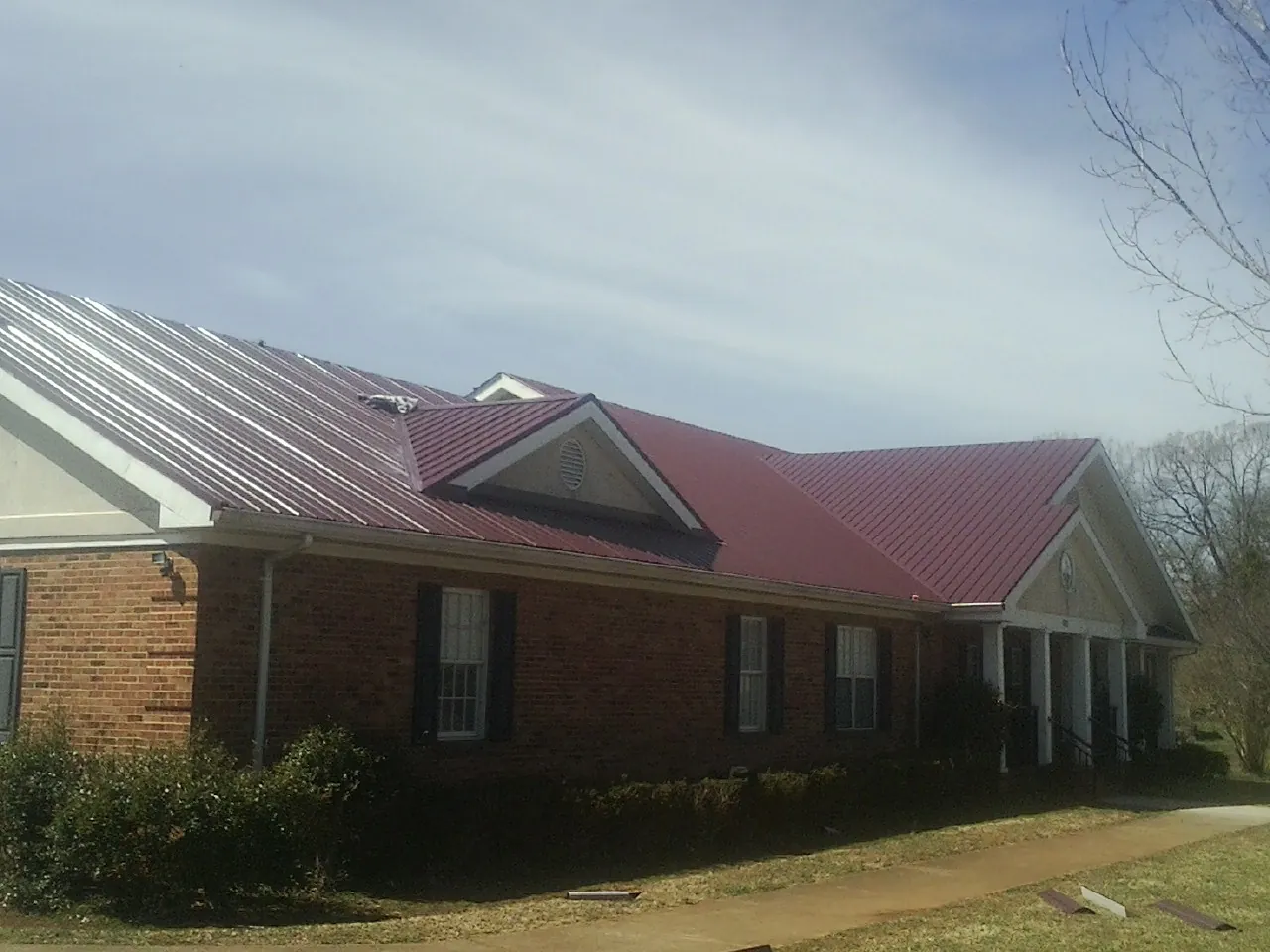 Red metal roof with gabled entries on a long brick building, from a Hail Damage Roof Repair job in Warrington