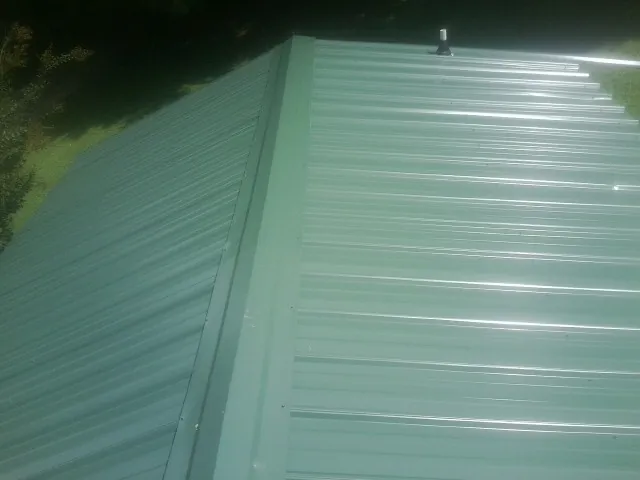 New green metal panels meeting at the ridge of a roof — Flat Roof Repair work by our crew in Warrington