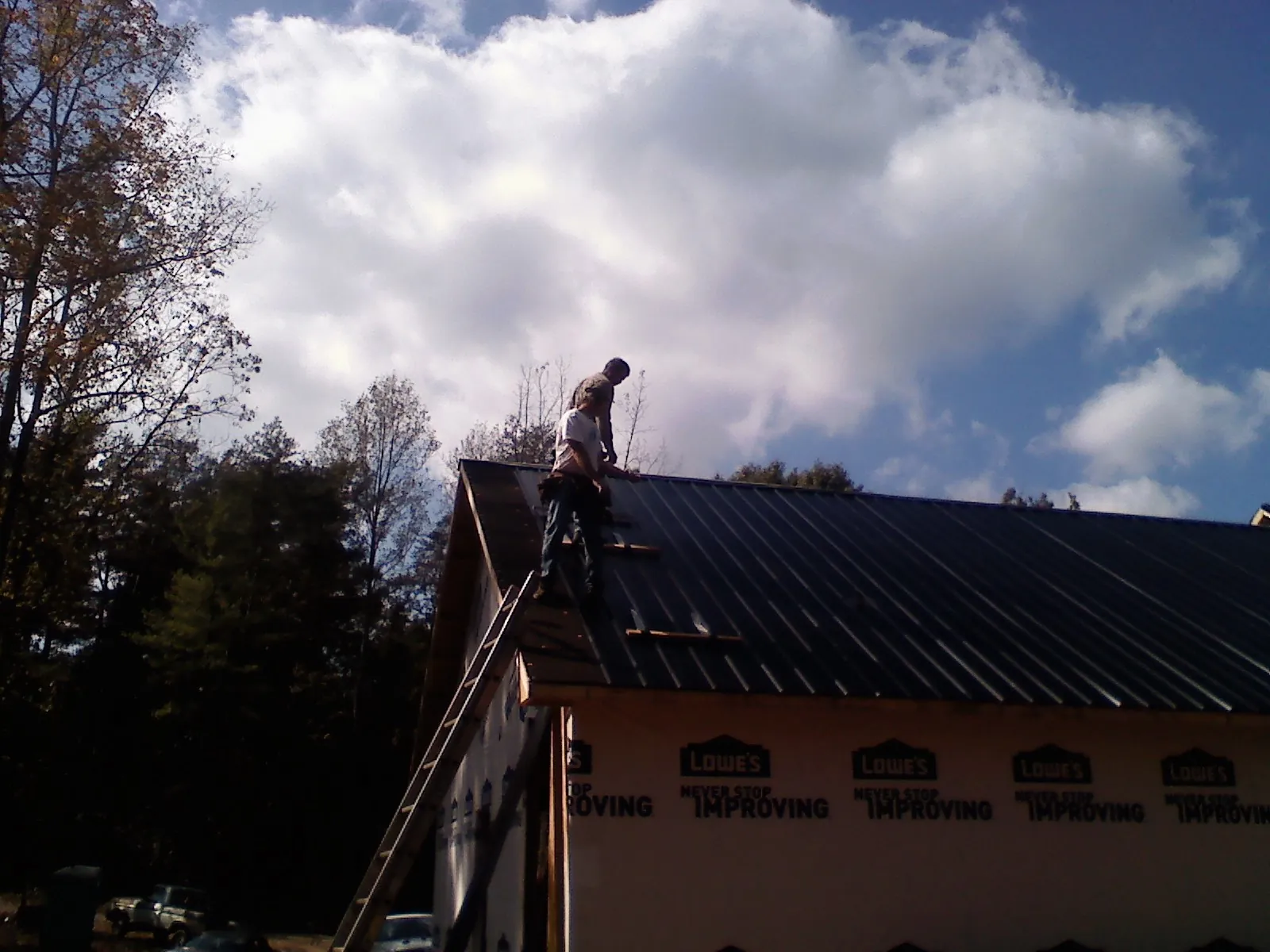 Roofer fastening dark metal panels high against a cloudy sky, from a Roof Inspection job in Warrington