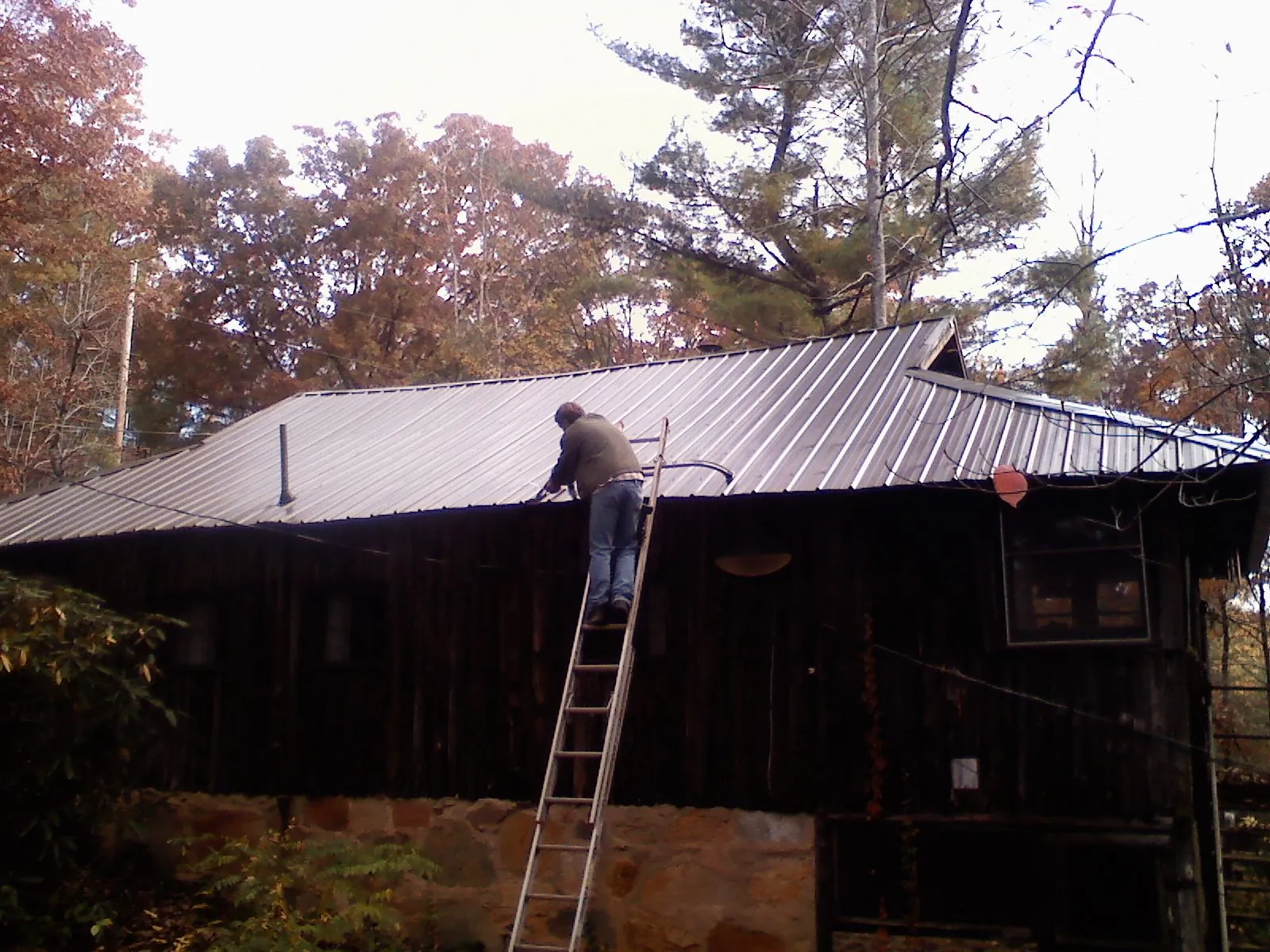 Roofer on a ladder working along the edge of a cabin metal roof in Warrington