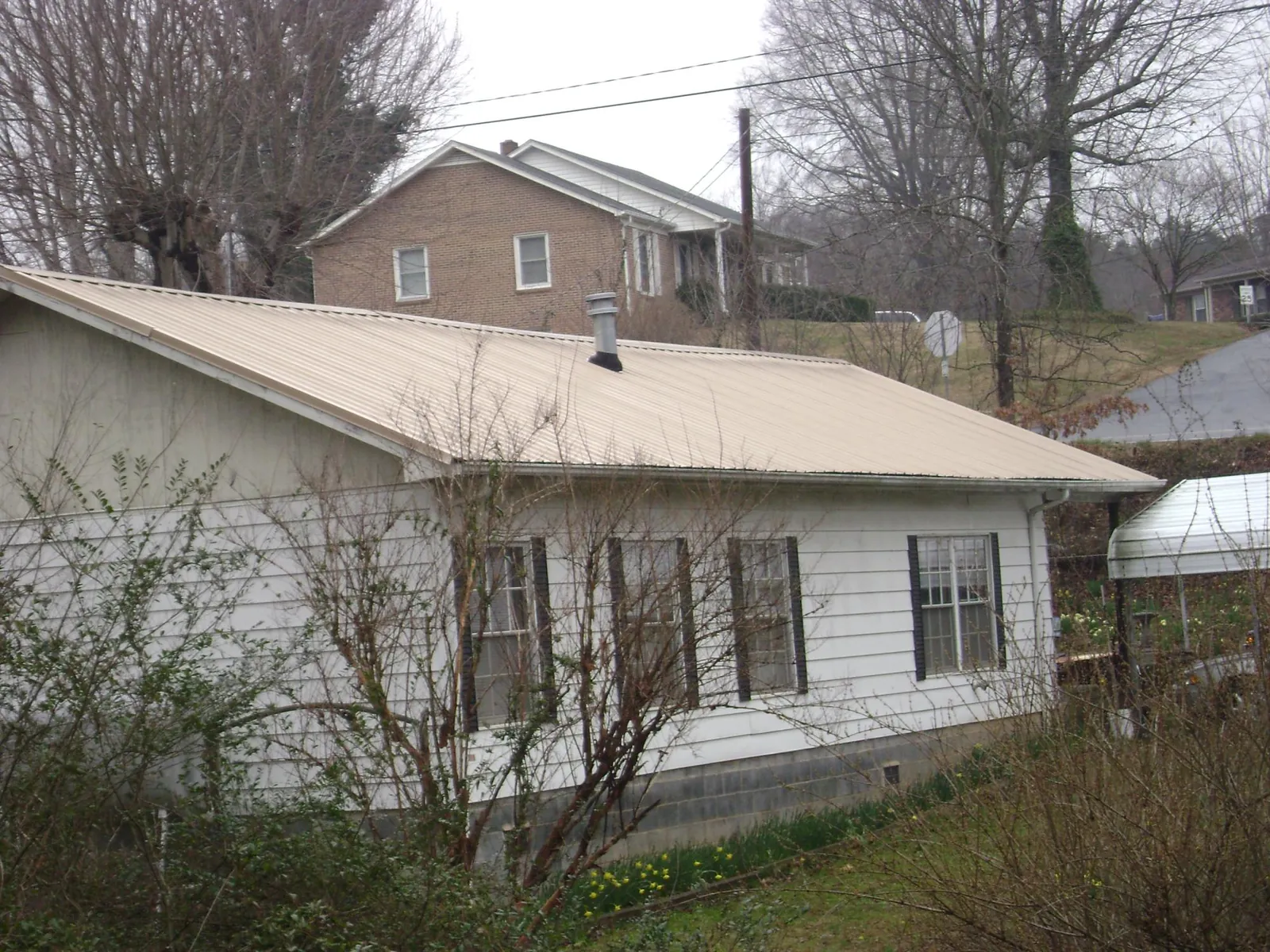 Tan metal roof on a white sided house set into a hillside — Commercial Roofing by Roofing Brothers in Warrington
