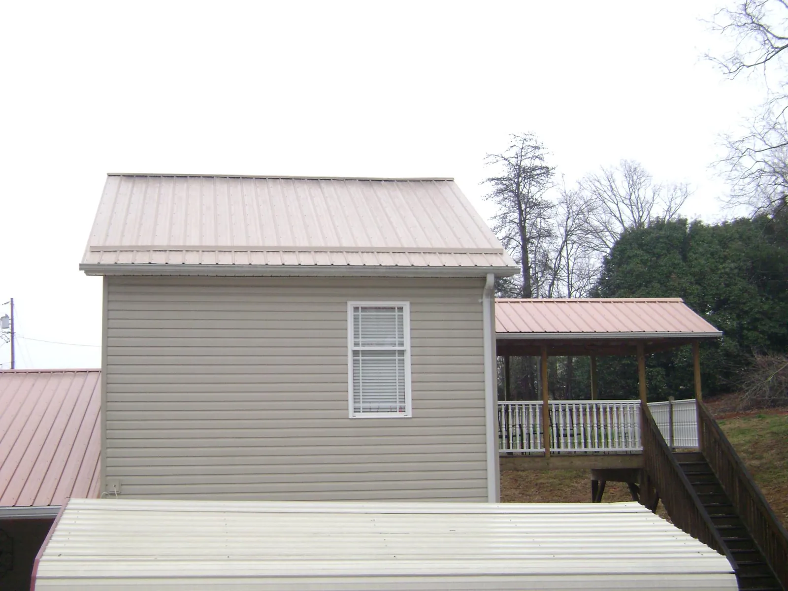 Tan metal roofs on a two story addition and attached porch, from a Roof Replacement job in Warrington